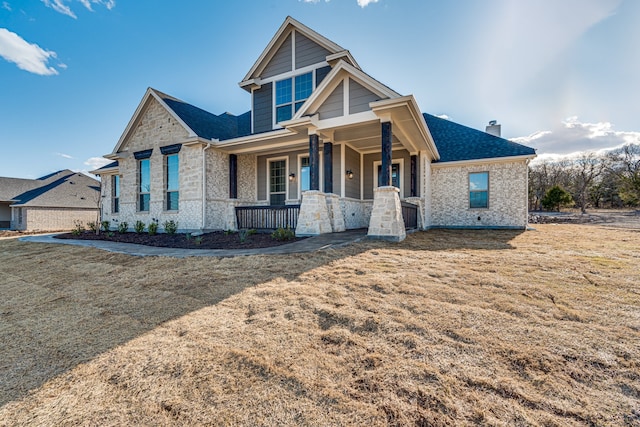 craftsman-style house with a porch, stone siding, roof with shingles, and a chimney