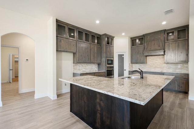 kitchen featuring visible vents, arched walkways, custom range hood, stainless steel appliances, and a sink