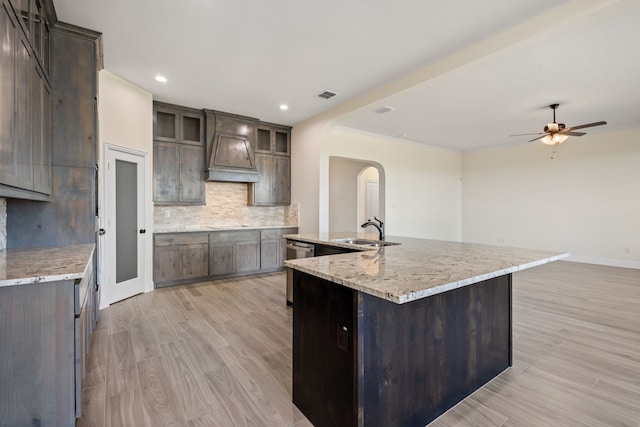 kitchen featuring arched walkways, a sink, visible vents, custom exhaust hood, and tasteful backsplash