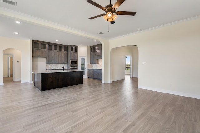 kitchen featuring dark brown cabinetry, tasteful backsplash, arched walkways, open floor plan, and light countertops