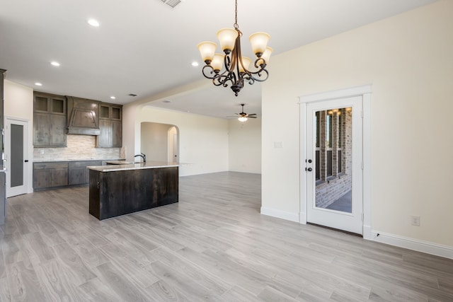 kitchen with arched walkways, light countertops, backsplash, dark brown cabinetry, and premium range hood