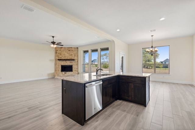 kitchen featuring visible vents, stainless steel dishwasher, light wood-type flooring, a brick fireplace, and light stone countertops