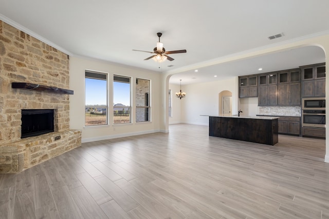 unfurnished living room with arched walkways, a stone fireplace, ceiling fan with notable chandelier, visible vents, and light wood-type flooring