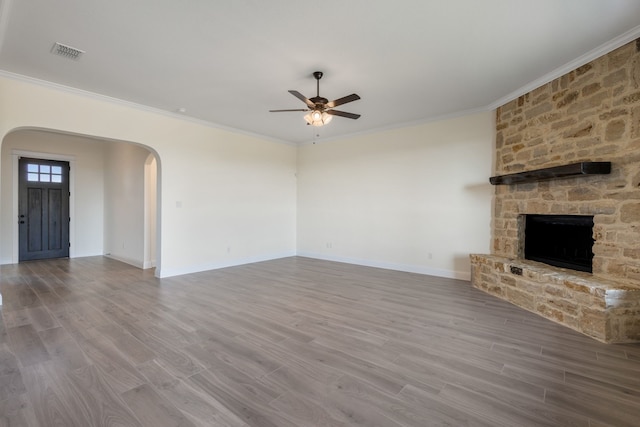 unfurnished living room with a ceiling fan, arched walkways, wood finished floors, and a stone fireplace