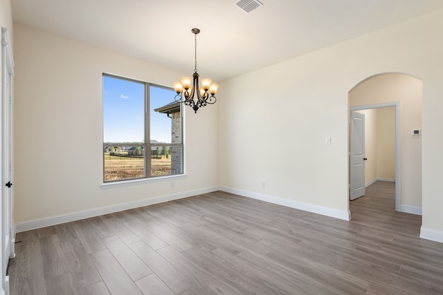 empty room with arched walkways, wood finished floors, visible vents, and a notable chandelier