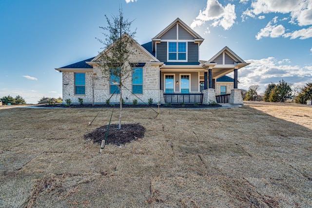 view of front of house with covered porch, stone siding, and a front lawn