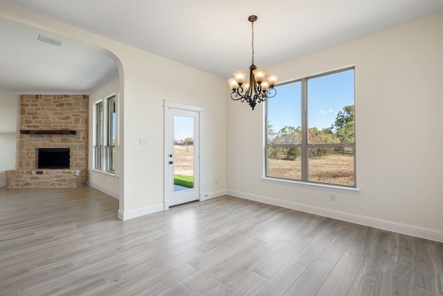 unfurnished dining area featuring light wood finished floors, baseboards, visible vents, arched walkways, and a fireplace