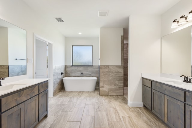 full bath featuring a freestanding tub, visible vents, a sink, and tile walls