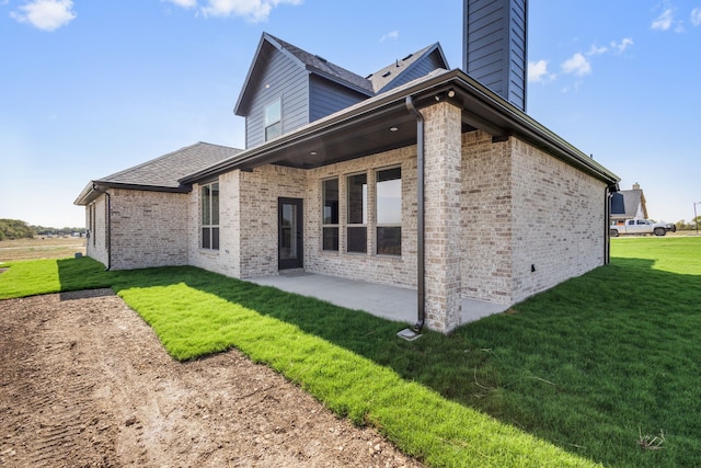 rear view of property featuring a patio area, a chimney, a lawn, and brick siding