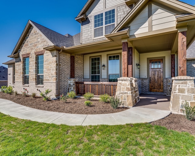 view of front facade featuring covered porch, stone siding, brick siding, and a shingled roof