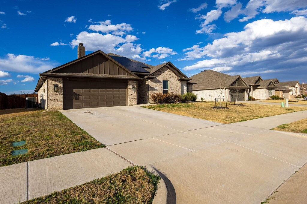 view of front of home with a garage, driveway, a chimney, roof mounted solar panels, and brick siding