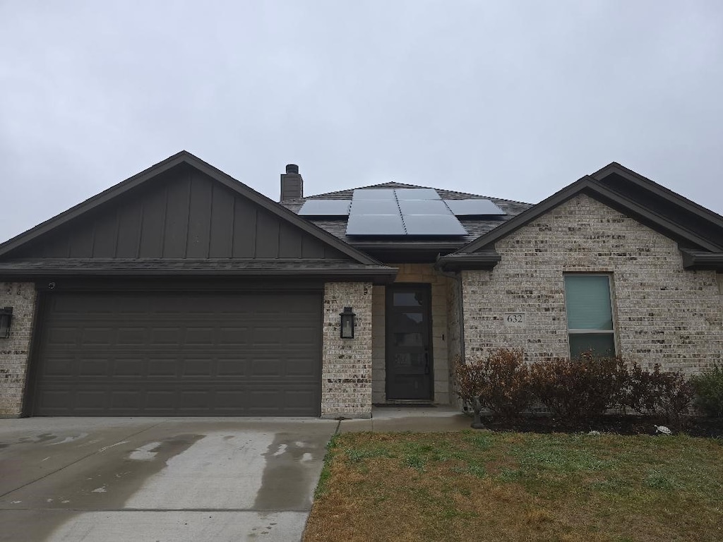 view of front facade with an attached garage, roof mounted solar panels, concrete driveway, and brick siding