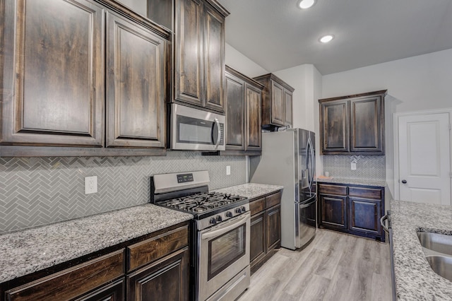 kitchen with dark brown cabinetry, light stone counters, decorative backsplash, light wood-style flooring, and appliances with stainless steel finishes