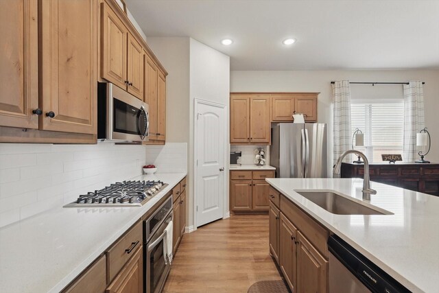 kitchen featuring stainless steel appliances, light countertops, backsplash, light wood-style floors, and a sink