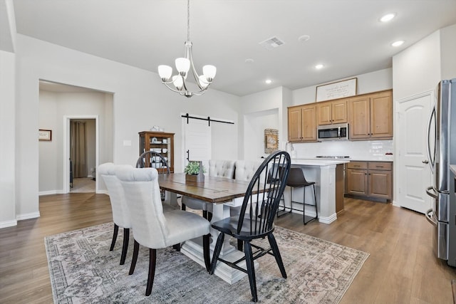 dining space with a chandelier, a barn door, recessed lighting, wood finished floors, and visible vents