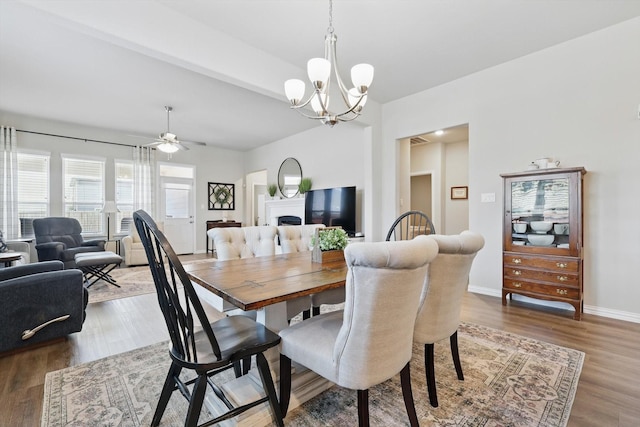 dining area with ceiling fan with notable chandelier, a fireplace, wood finished floors, and baseboards