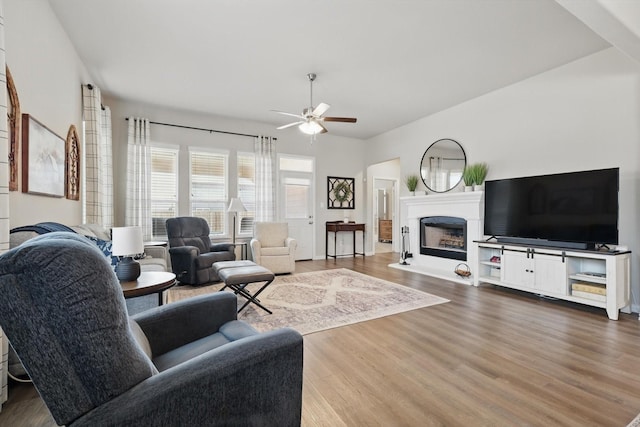 living room with ceiling fan, a fireplace with raised hearth, and dark wood-style flooring