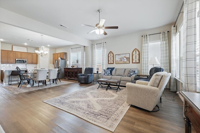 living area with ceiling fan with notable chandelier, visible vents, and wood finished floors