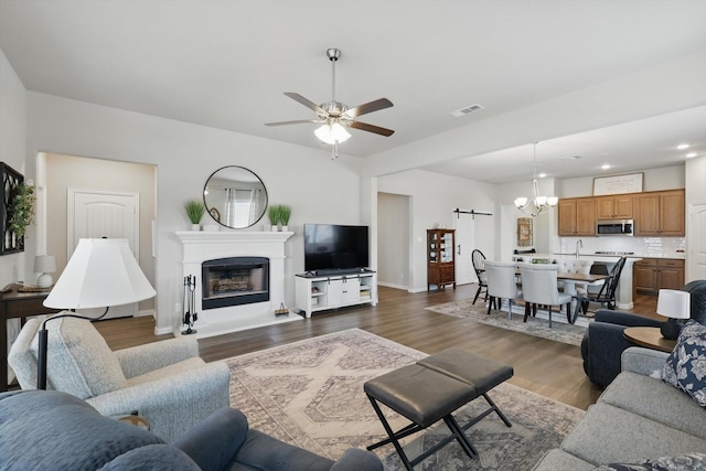 living room with dark wood-style floors, a fireplace, visible vents, a barn door, and ceiling fan with notable chandelier