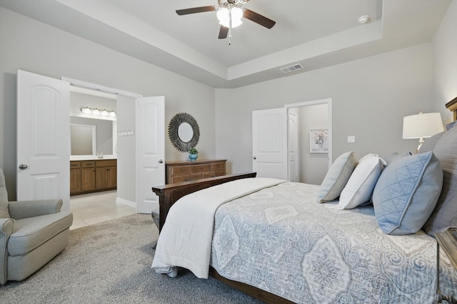 bedroom featuring a tray ceiling, visible vents, connected bathroom, and light carpet