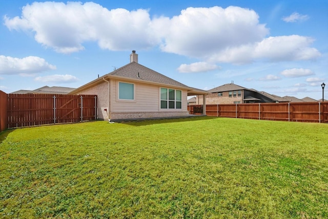 back of house featuring a fenced backyard, a chimney, a lawn, and brick siding