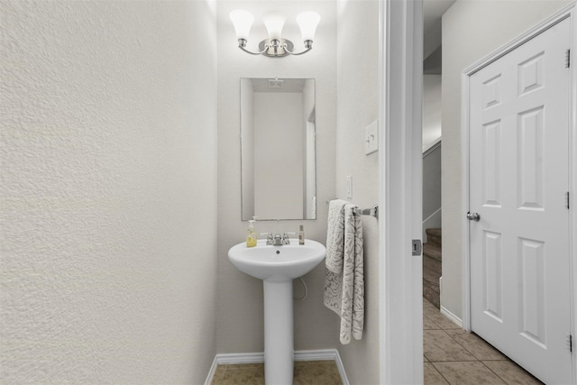 bathroom featuring baseboards, a textured wall, an inviting chandelier, and tile patterned floors