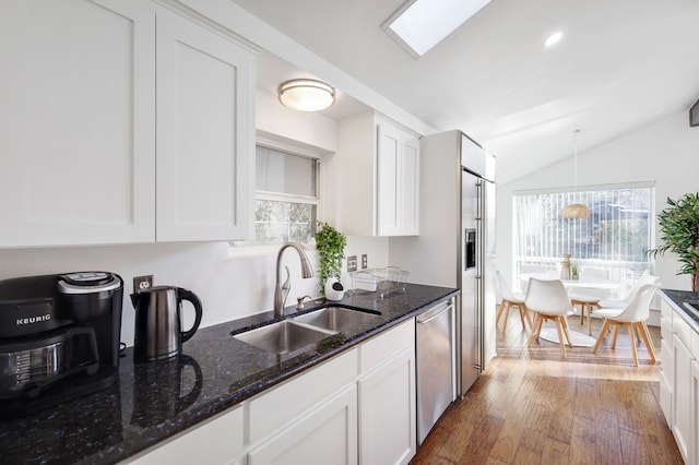 kitchen featuring vaulted ceiling with skylight, hardwood / wood-style flooring, a sink, white cabinetry, and dishwasher