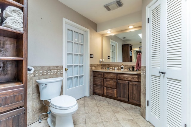 bathroom featuring visible vents, toilet, vanity, tile patterned floors, and tile walls