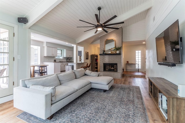 living area featuring ceiling fan, beamed ceiling, light wood-type flooring, wooden ceiling, and a fireplace