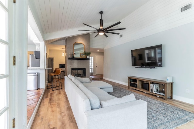 living area with lofted ceiling, a brick fireplace, a healthy amount of sunlight, and visible vents