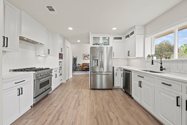 1607 Amesbury Ln, Rockwall, TX 75087 - kitchen with stainless steel appliances, a sink, light wood-style floors, tasteful backsplash, and white cabinets