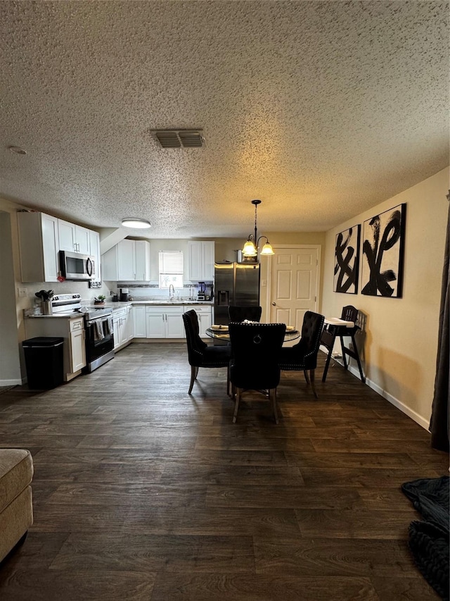 dining area with a chandelier, a textured ceiling, dark wood-type flooring, visible vents, and baseboards