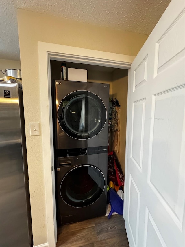 clothes washing area with stacked washer / drying machine, dark wood-style flooring, a textured ceiling, and laundry area