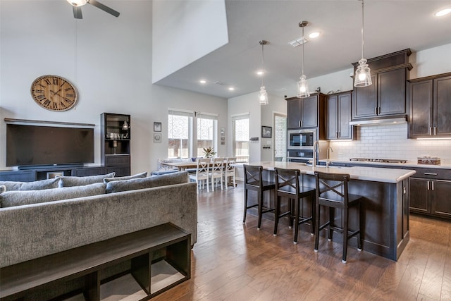 kitchen with dark brown cabinetry, open floor plan, a breakfast bar, appliances with stainless steel finishes, and dark wood-style floors