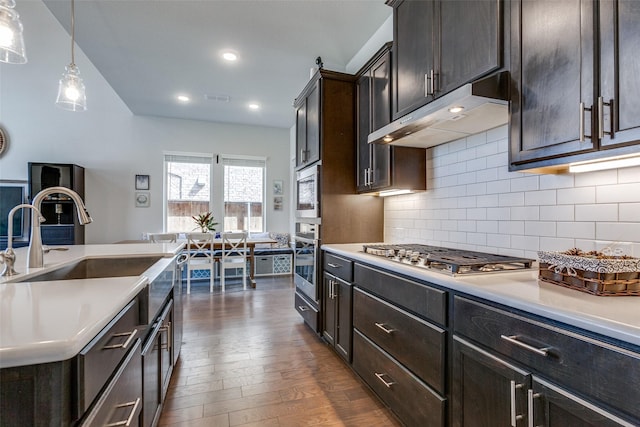 kitchen featuring under cabinet range hood, light countertops, decorative backsplash, stainless steel appliances, and dark wood-style flooring