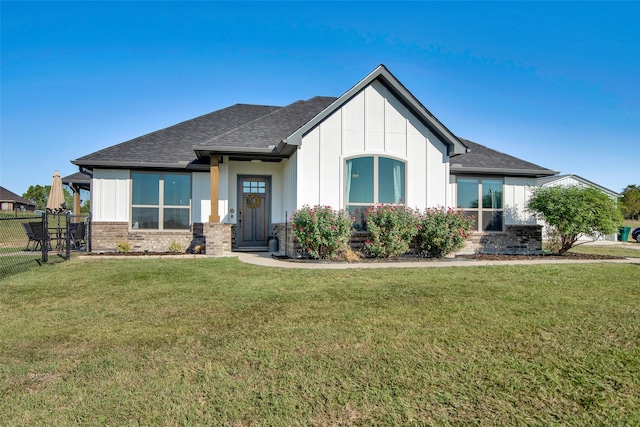 view of front of home with brick siding, a shingled roof, fence, board and batten siding, and a front yard