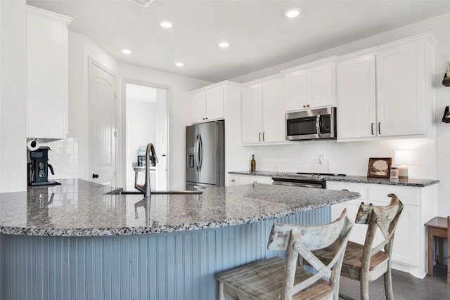 kitchen featuring stainless steel appliances, white cabinetry, a sink, dark stone countertops, and a peninsula