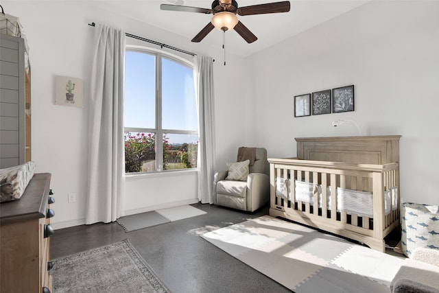 bedroom featuring a ceiling fan, a nursery area, and baseboards