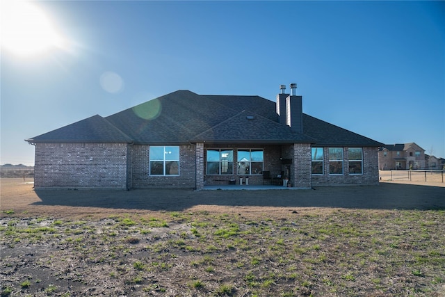 rear view of property featuring a shingled roof, a patio area, brick siding, and a chimney