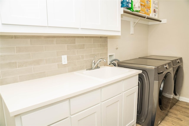 washroom with a sink, baseboards, light wood-style floors, cabinet space, and washer and clothes dryer