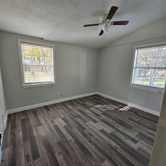 empty room featuring dark wood-style floors, baseboards, vaulted ceiling, and a wealth of natural light