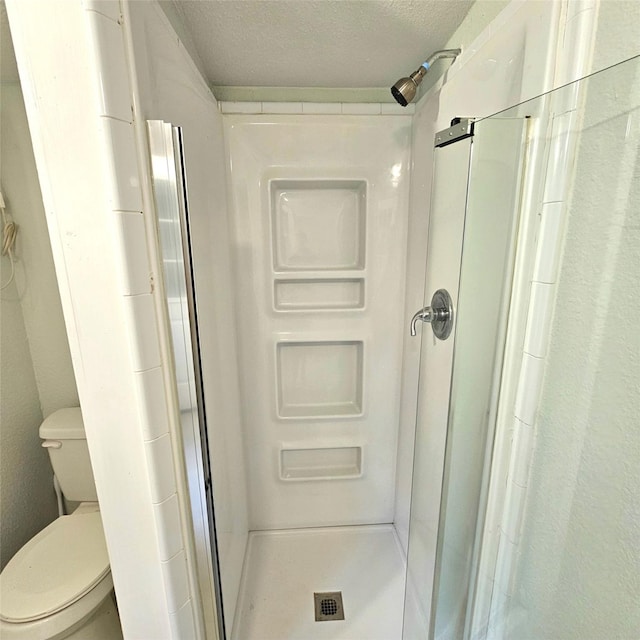 bathroom featuring toilet, a stall shower, and a textured ceiling