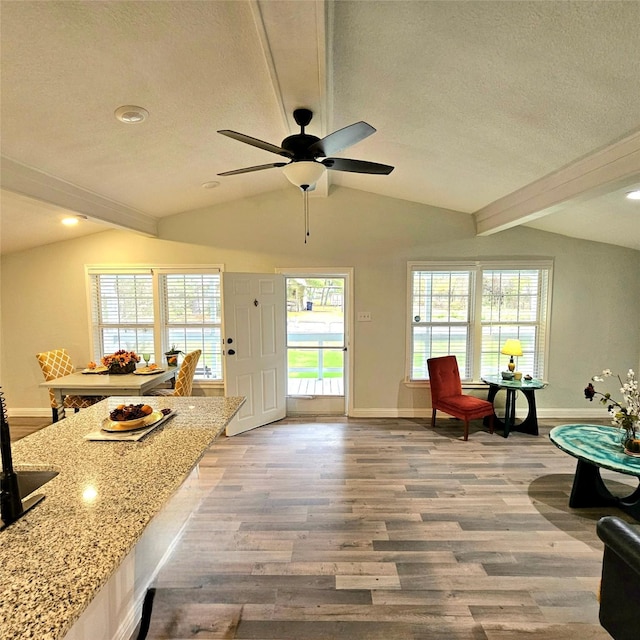 interior space with lofted ceiling with beams, a textured ceiling, wood finished floors, and light stone countertops