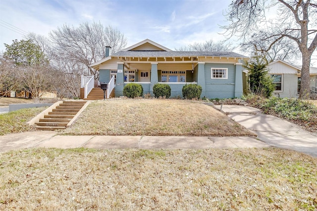 view of front of property with brick siding, a chimney, a porch, stairway, and a front yard