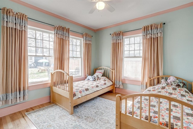 bedroom with ornamental molding, multiple windows, wood finished floors, and baseboards