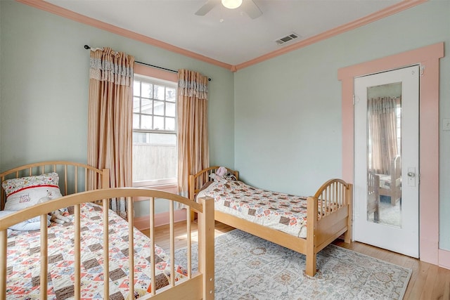 bedroom featuring a ceiling fan, crown molding, visible vents, and wood finished floors