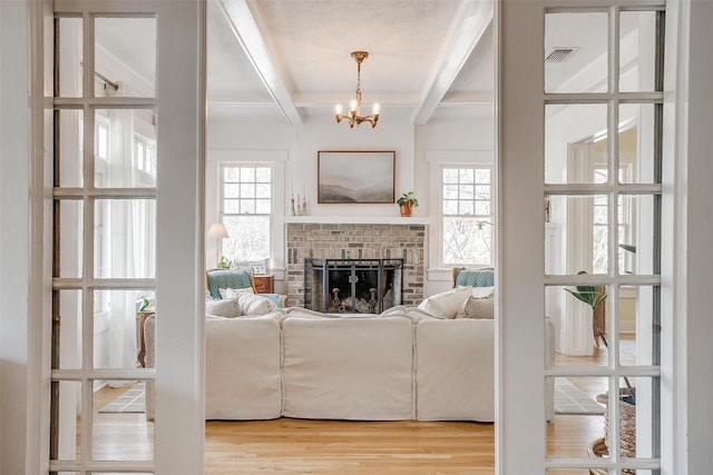 living area featuring a wealth of natural light, a brick fireplace, wood finished floors, and beamed ceiling