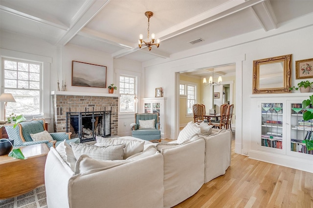 living area with a brick fireplace, light wood-type flooring, visible vents, and a notable chandelier