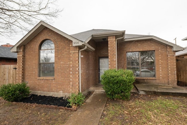 view of front of property with brick siding, fence, and roof with shingles