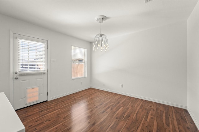 unfurnished dining area with dark wood-style floors, baseboards, and an inviting chandelier